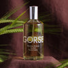 Lifestyle shot of Laboratory Perfumes Gorse Eau de Toilette on dark brown linen cloth with green stalks in the background