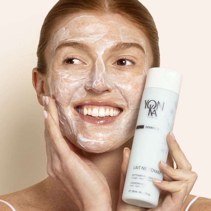 Model holding bottle of Yon-Ka Paris Lait Nettoyant (200 ml) with product applied to face