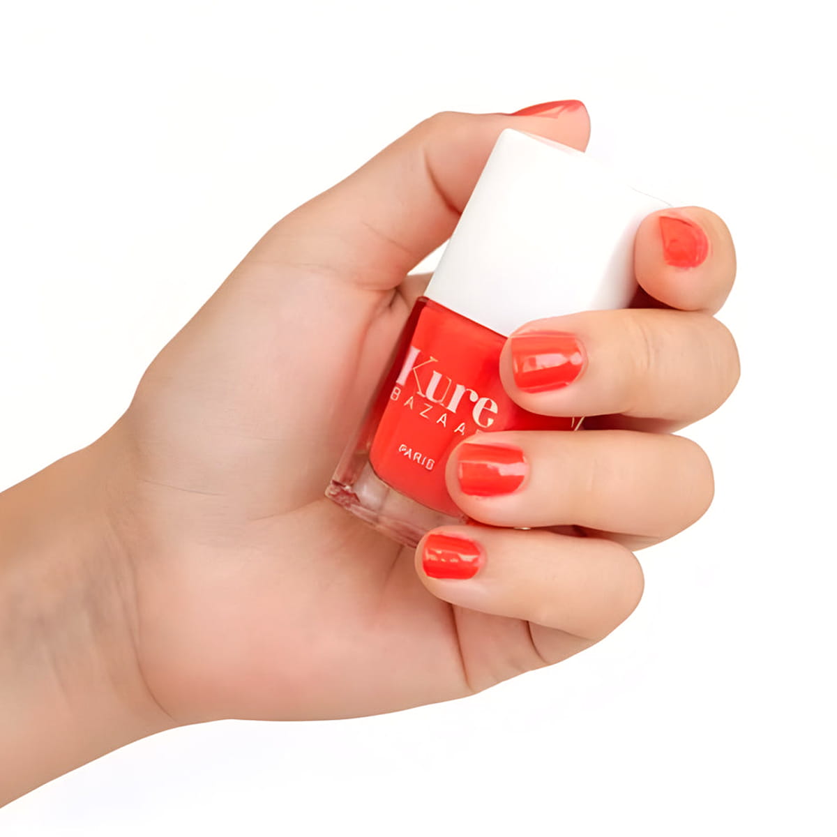 Close up of model wearing Kure Bazaar Nail Lacquer - Coquette (10 ml) and holding bottle