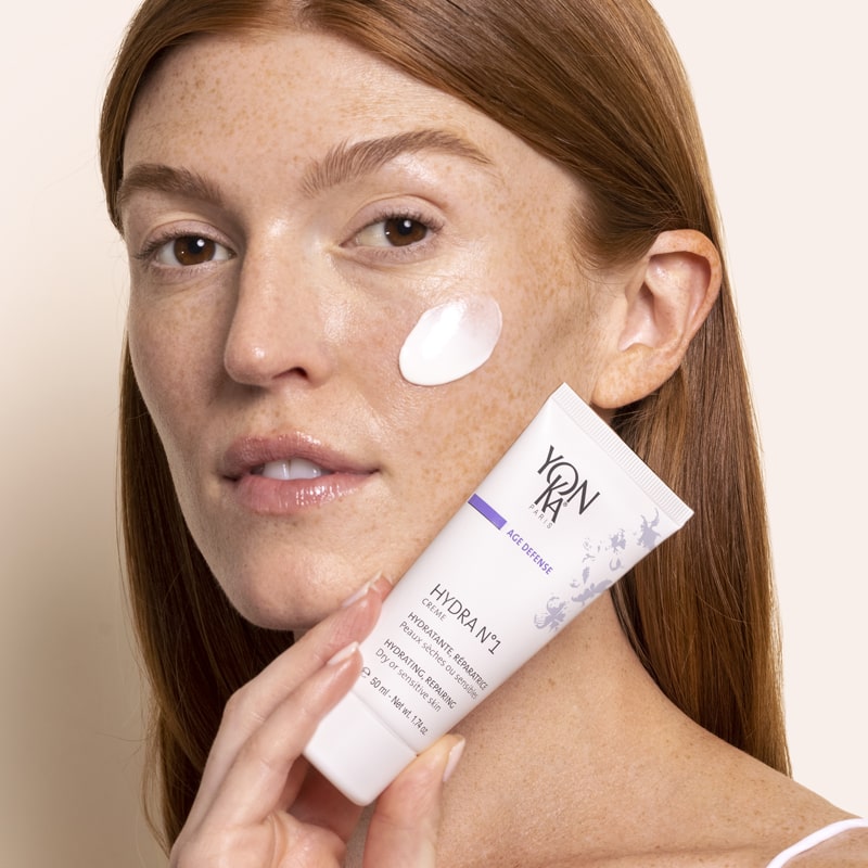Model holding tube of Yon-Ka Paris Hydra No. 1 Creme (50 ml) with product smear on cheek to show color and texture
