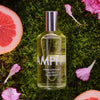 Lifestyle shot top view of Laboratory Perfumes Samphire Eau de Toilette on grass with pink flowers and grapefruit in the background