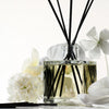 Kai Fragrance Reed Diffuser (6.75 oz) surrounded by white flowers on a light background