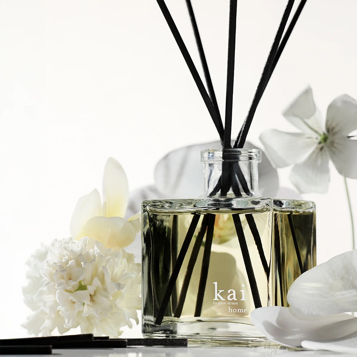 Kai Fragrance Reed Diffuser (6.75 oz) surrounded by white flowers on a light background
