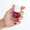 Close up of model wearing and holding bottle of Kure Bazaar Nail Lacquer - Amore (10 ml)