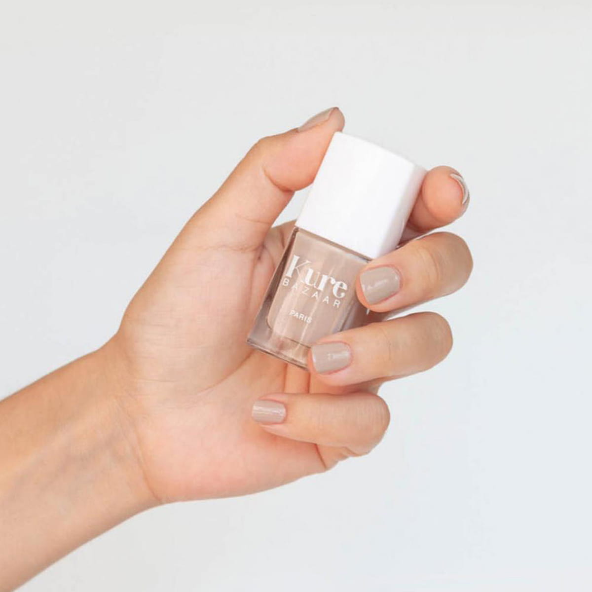 Close up of model wearing Kure Bazaar Nail Lacquer - Nude (10 ml) and holding bottle
