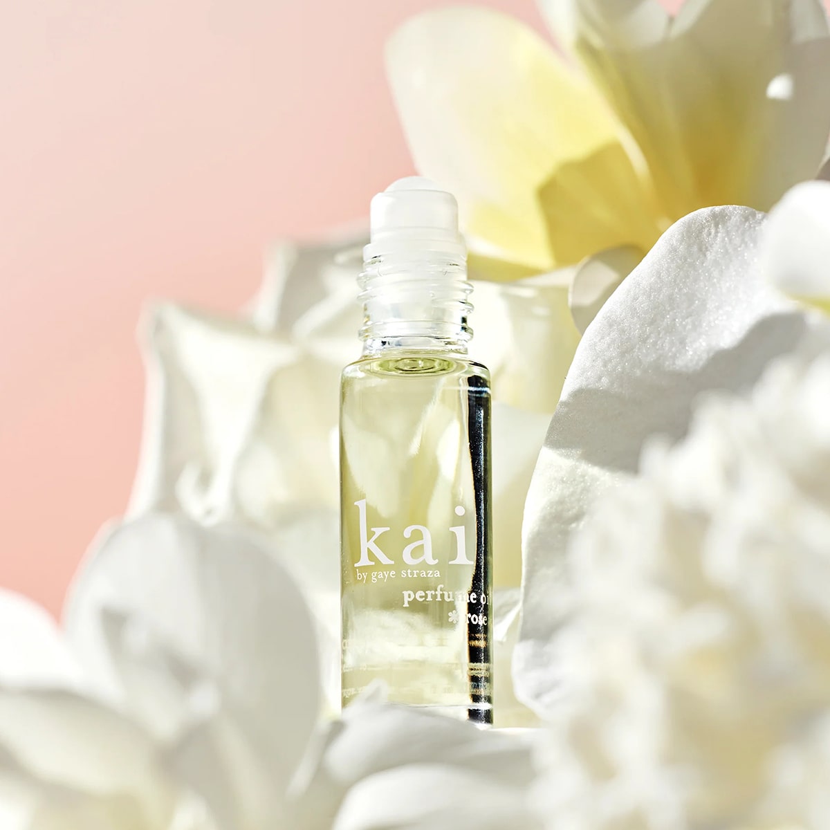 Kai Fragrance Rose Perfume Oil (1/8 oz) surrounded by white flowers on a pink background