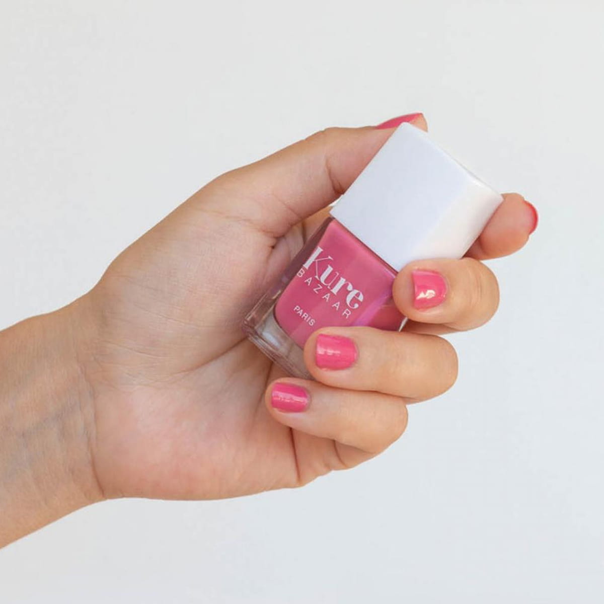Close up of model wearing Kure Bazaar Nail Lacquer - Sunset (10 ml) and holding bottle