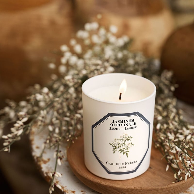 Lifestyle shot of Carriere Freres Jasmine Candle (185 g) shown lit with white flowers in the background