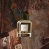 Image of Trudon Bruma Eau de Parfum (100 ml) with illustration of wall hangings, tapestry and chandelier in the background