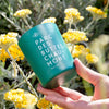 Kerzon Fragranced Candle - Parc des Buttes-Chaumont (190 g) - product shown being held in front of flowers.