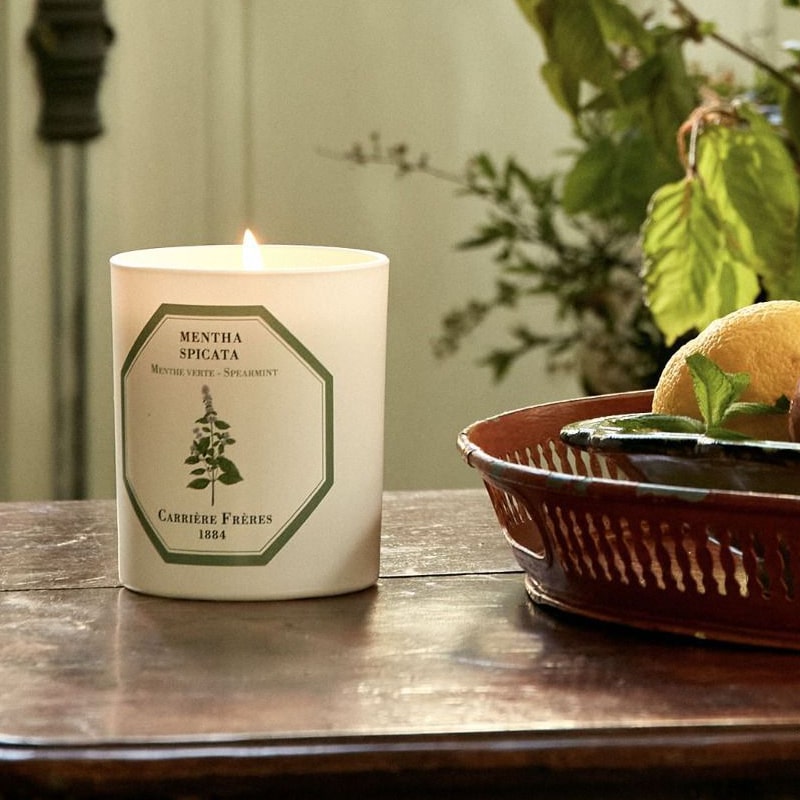 Lifestyle shot of Carriere Freres Spearmint Candle (185 g) shown lit on wood table with basket in the background with lemon