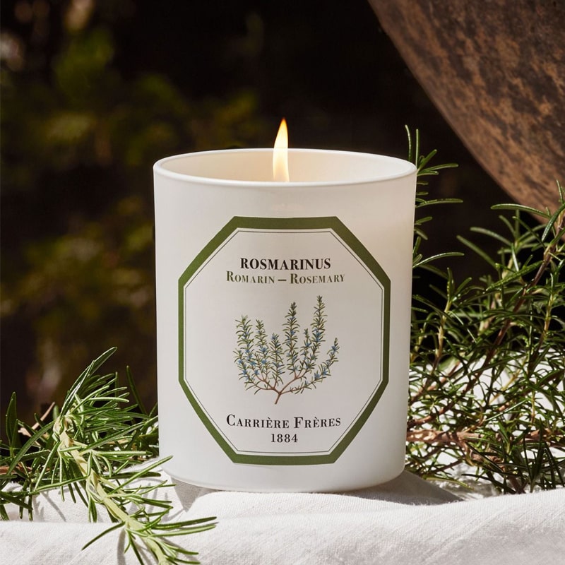 Lifestyle shot of Carriere Freres Rosemary Candle (185 g) shown lit with rosemary in the background