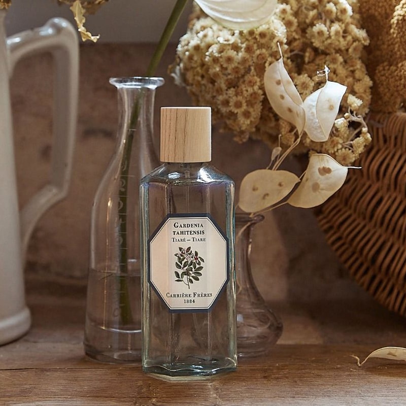 Lifestyle shot of Carriere Freres Tiare Room Spray (200 ml) with glass vases and dried flowers in the background