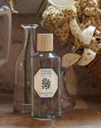 Lifestyle shot of Carriere Freres Tiare Room Spray (200 ml) with glass vases and dried flowers in the background