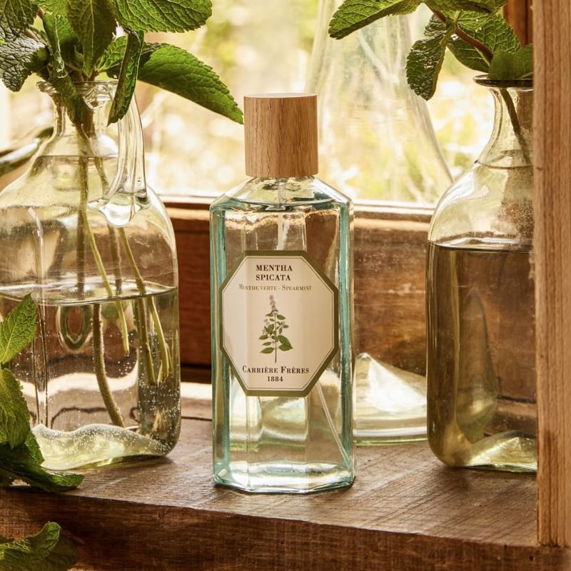 Lifestyle shot of Carriere Freres Spearmint Room Spray (200 ml) on window sill with glass vases in the background