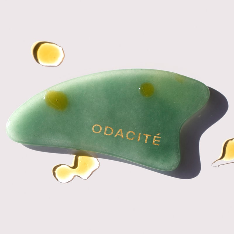 Odacite Crystal Contour Gua Sha Green Adventurine Beauty Tool shown with oil drops on and around tool