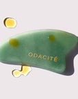 Odacite Crystal Contour Gua Sha Green Adventurine Beauty Tool shown with oil drops on and around tool