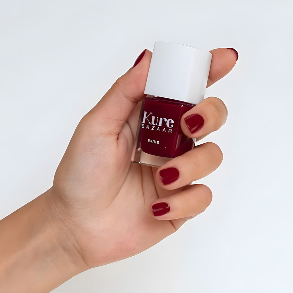 Close up of model wearing and holding bottle of Kure Bazaar Nail Lacquer - Vogue (10 ml)