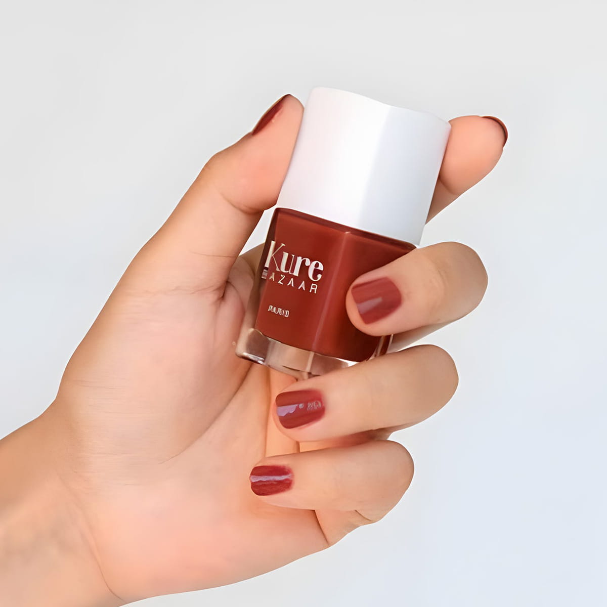Close up of model wearing and holding  bottle of Kure Bazaar Nail Lacquer - Blush (10 ml)