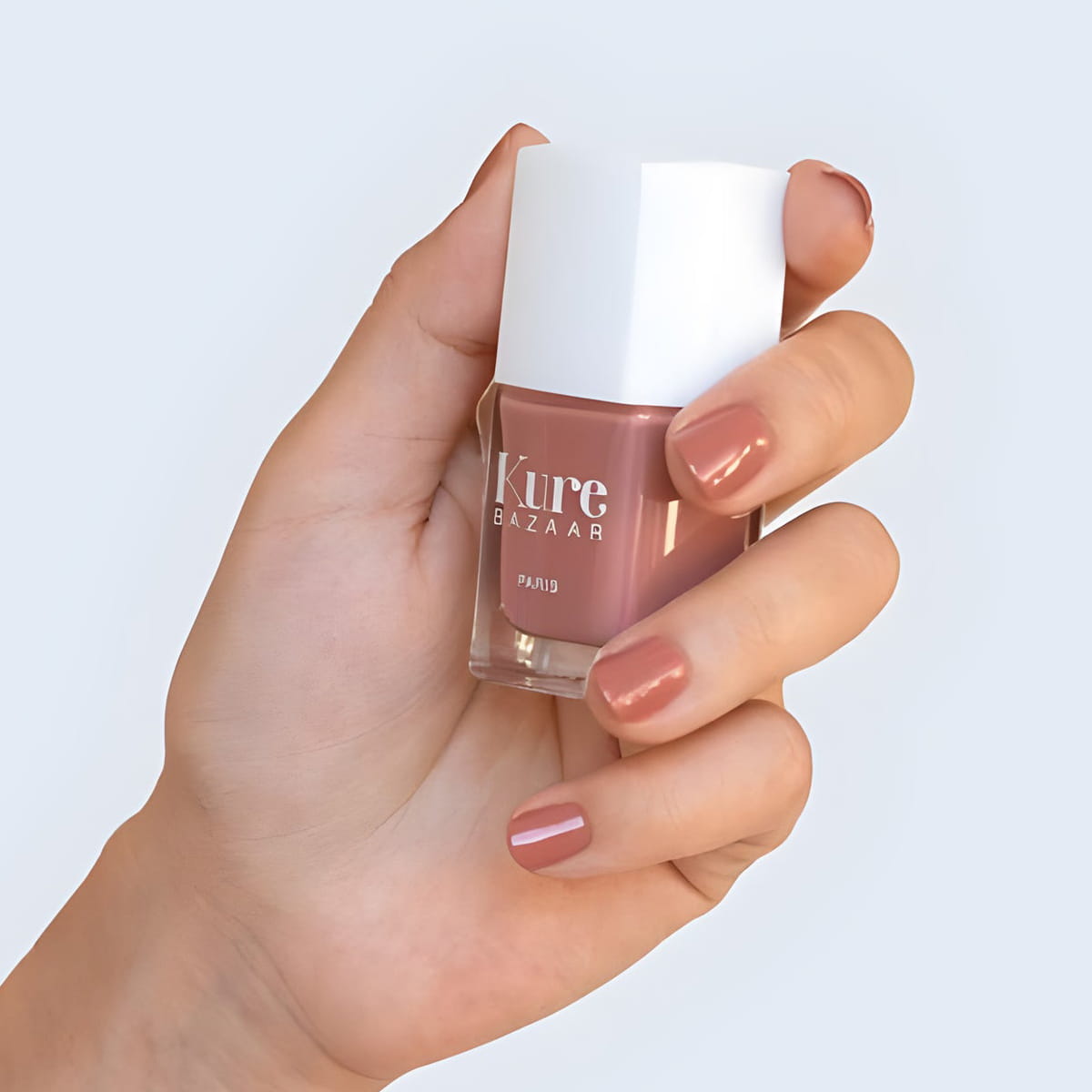 Close up of model wearing Kure Bazaar Nail Lacquer - Zoe (10 ml) and holding bottle