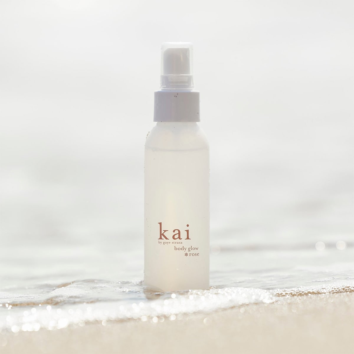 Kai Fragrance Rose Body Glow (4 oz) shown on beach with water
