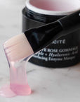 Close up of Odacite Bioactive Rose Gommage (50ml) jar in the background and brush covered with rose gommage