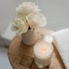 Kai Fragrance Rose Skylight Candle (10 oz) and vase with white roses on a wooden surface