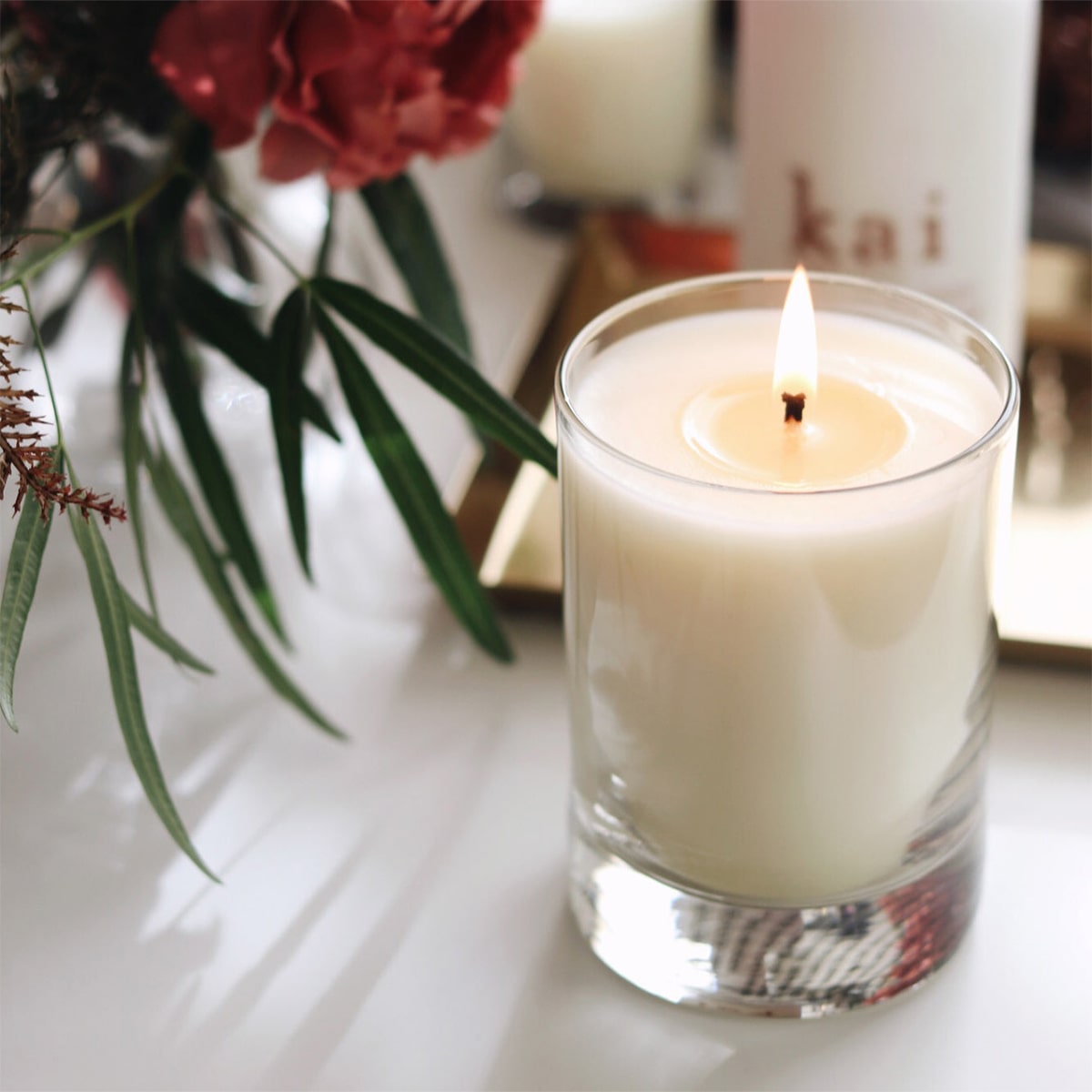 Kai Fragrance Rose Skylight Candle (10 oz) with flowers and a blurred background
