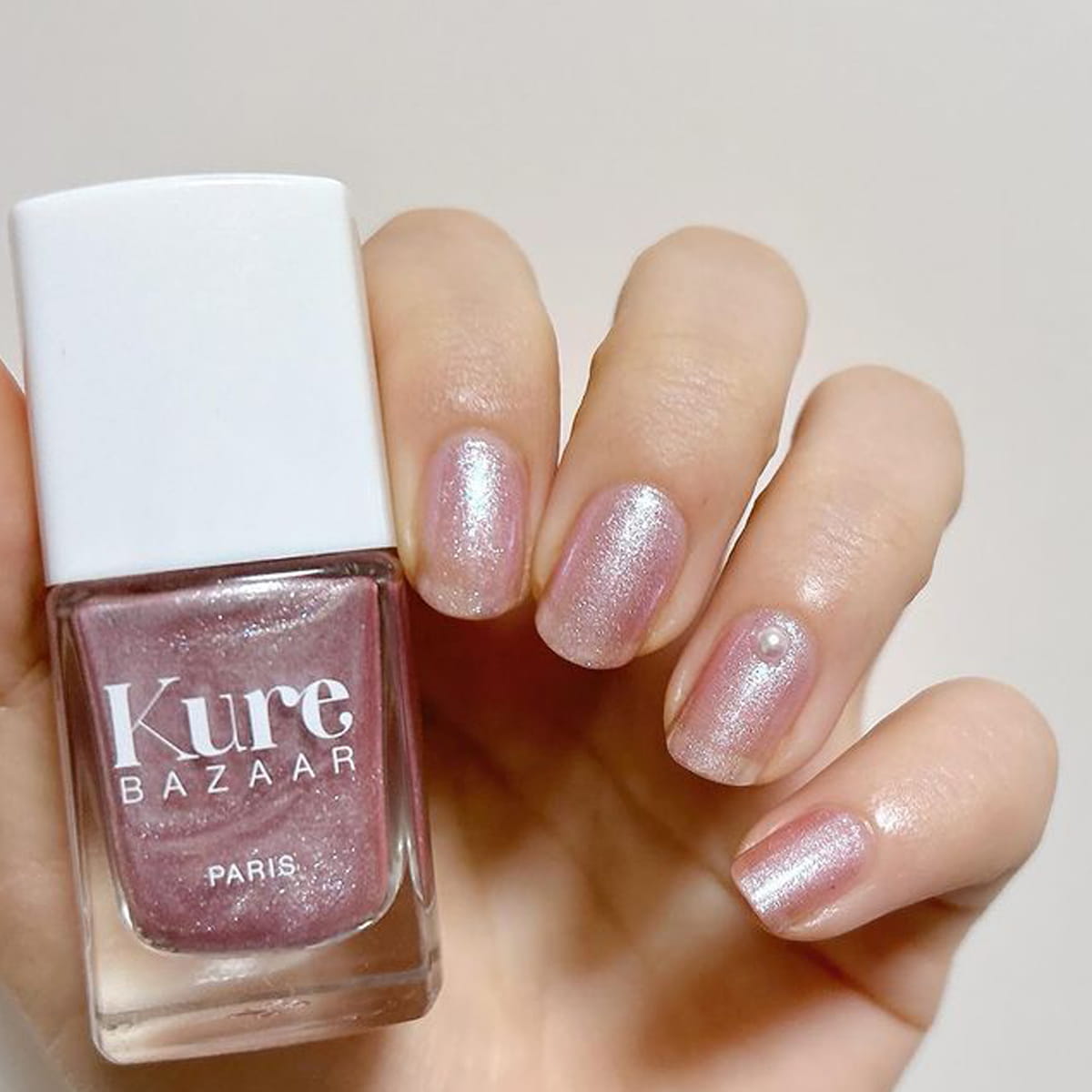 Close up of model wearing Kure Bazaar Nail Lacquer - Flamingo (10 ml) and holding bottle