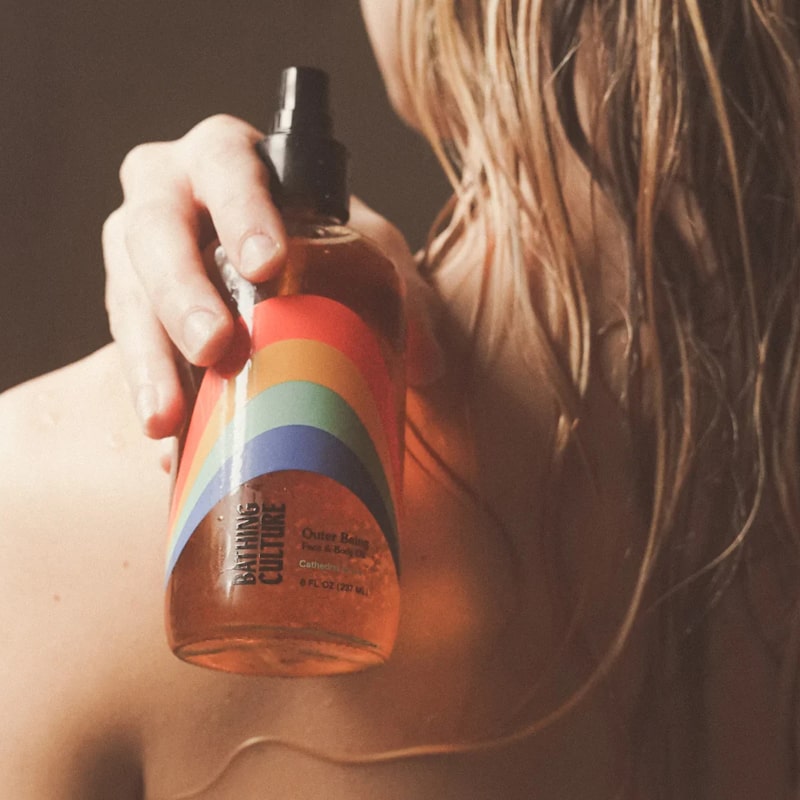 Lifestyle shot of Bathing Culture Outer Being Face &amp; Body Oil (8 oz) with model holding bottle over her shoulder