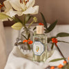 Lifestyle shot of Carriere Freres Orange Blossom Room Spray (200 ml) with flowers in the background