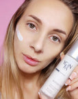 Model holding bottle of Yon-Ka Paris Alpha Fluid (50 ml) and product smear on cheek to show color and texture
