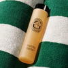 Lifestyle shot of Diptyque Revitalizing Shower Gel (200 ml) bottle sitting on green and white striped towel