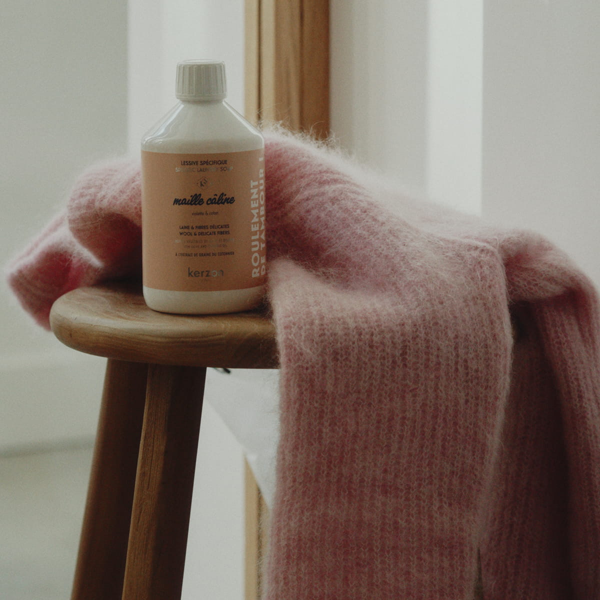 Kerzon Laundry Soap - Maille Caline (500 ml) - product shown on stool next to pink wool sweater. 