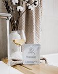 Bathorium Sea Kelp Serenity Crush Bath Soak - packaging on wood tray with glass of wine, towel, and vase with cotton
