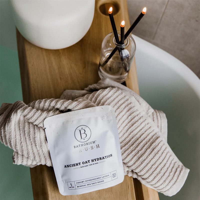 Bathorium Ancient Oat Hydration Crush Bath Soak - packaging on wood tray over bathtub with candles and towel