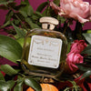 Lifestyle shot of Santa Maria Novella Rosa Novella Cologne (100 ml) with pink roses, leaves and citrus in the background