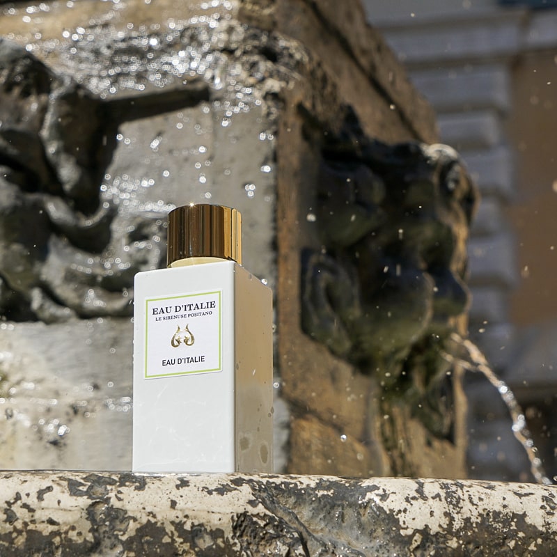 Lifestyle shot of Eau d&#39;Italie Eau de Parfum Spray (100 ml) with stone fountain in the background