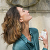 Model spraying Eau d'Italie Eau de Parfum (100 ml) on her neck with stone fountain in the background