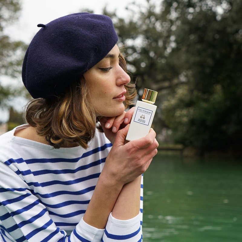 Lifestyle shot of model holding Eau d&#39;Italie Un Bateau Pour Capri Eau de Parfum Spray (100 ml) with lake in the background