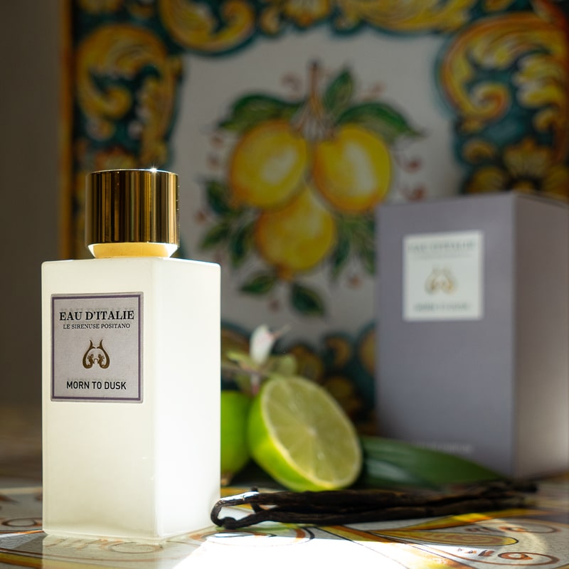 Lifestyle shot of Morn to Dusk Eau de Parfum Spray (100 ml) with box, vanilla pods and limes in the background