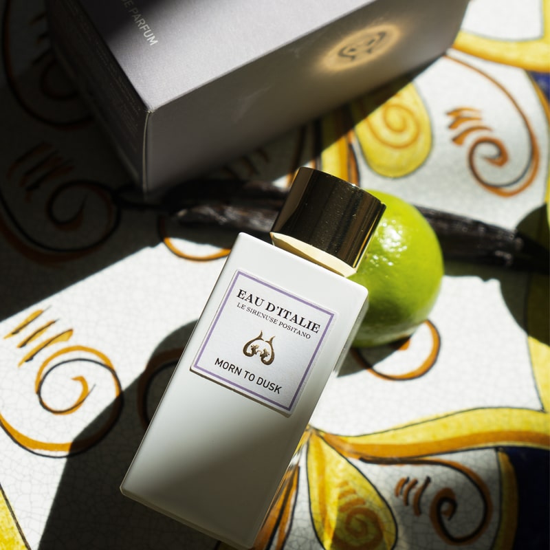 Lifestyle shot top view of Morn to Dusk Eau de Parfum Spray (100 ml) and box with decorative tile, lime and vanilla pod in the background