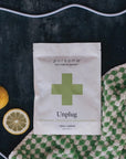 Pursoma Unplug Ritual - bath soak packaging next to lemons, towel, and rope on dark background