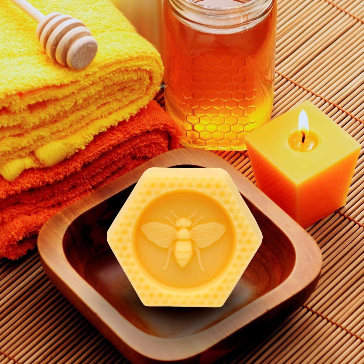 Lifestyle shot of Honey House Naturals Large Bee Bar Lotion - Natural (2 oz) on wood tray with honey in a glass jar and candle burning with folded towels in the background