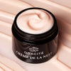 Lifestyle shot of Odacite Creme de la Nuit (50 ml) shown without lid to show cream with cream in the background
