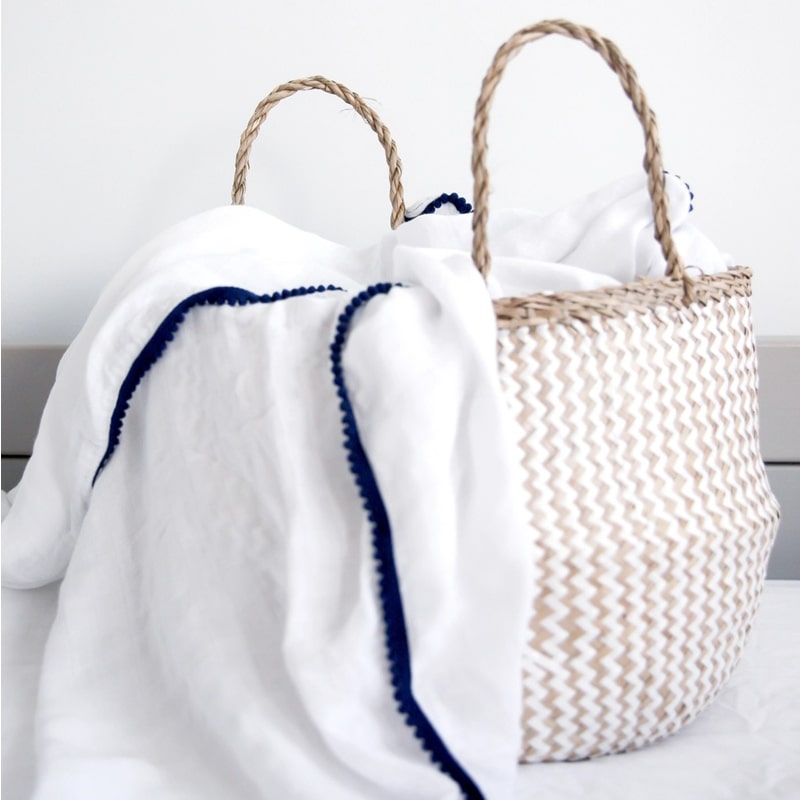 Lifestyle shot of Malabar Baby Luxe Silky Soft Bamboo Cotton Swaddle – Navy Pom Pom Trim (1 pc) shown in wicker handbag