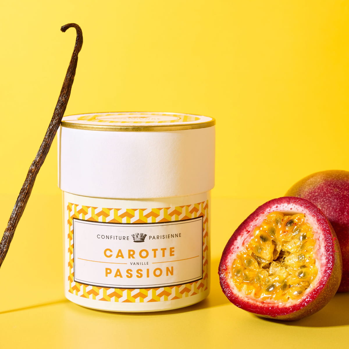 Confiture Parisienne Carrot - Passionfruit - Vanilla Jam (8.5 oz), styled with a vanilla bean and a halved passion fruit on a bright yellow background.