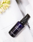 de Mamiel First Fix Stress Response Serum beauty shot pictured on a book with a flower nearby