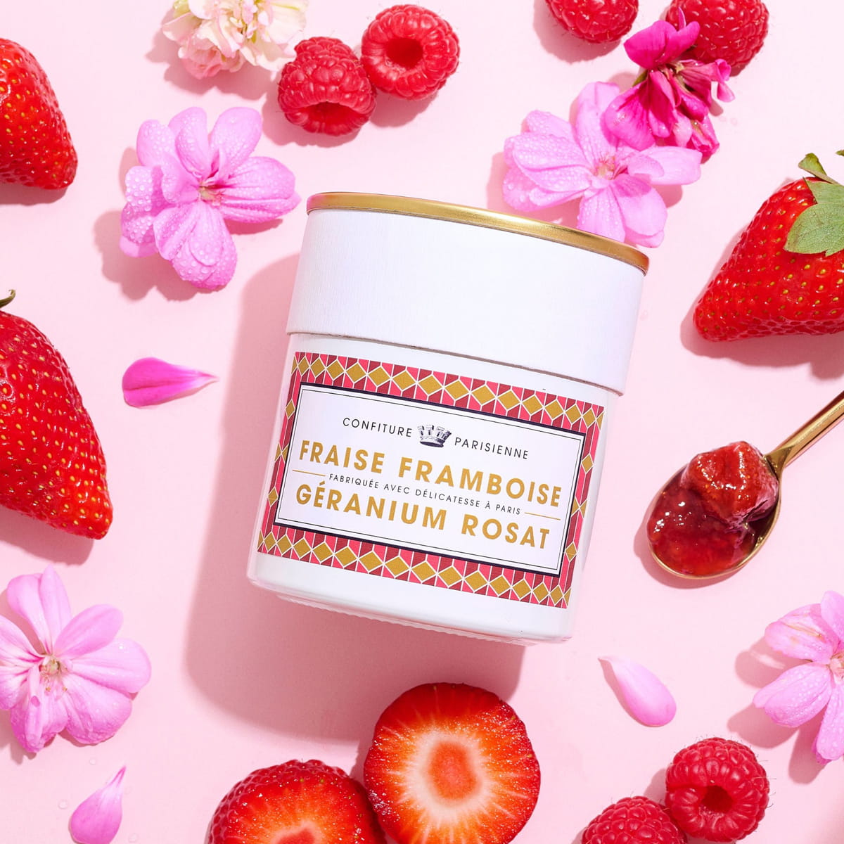 Confiture Parisienne Strawberry Raspberry Rose Geranium (8.8 oz) surrounded by strawberries, raspberries, pink flowers, and a gold spoon with jam on it.