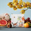 Storytiles Small Tile – Nathalie Lete Birds and Bees (1 pc) - product shown on blue background with foliage and fruit around. 